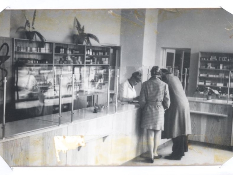 skan czarno-białego zdjęcia; na zdjęciu wnętrze apteki; przy kontuarze farmaceutka i dwoje klientów