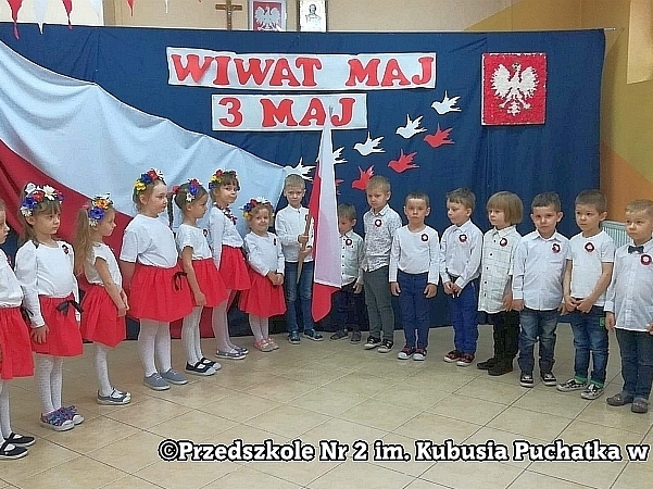 Dzieci ustawione są w półkolu w tle patriotycznej dekoracji