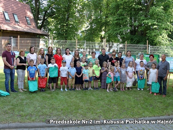 Grupa ludzi stoi na placy przy Hajnowskim Domu Kultury. W tle widać wystawę prac konkursowych.