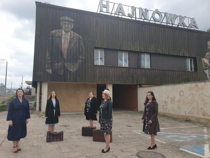 Pięć kobiet stoi przed budynkiem Hajnówki Centralnej. Obok stoją trzy stare walizki.