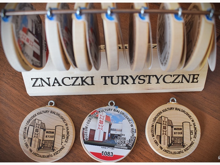 Na stole leżą trzy znaczki turystyczne. Dwa z tym samym wizerunkiem. 