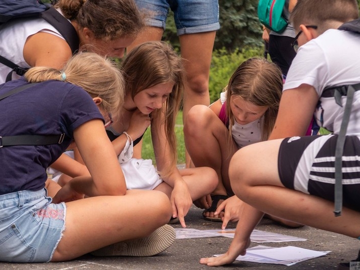 grupa młodzieży skupia się nad rozwiązaniem gry. Pokazują palcem możliwe rozwiązania.