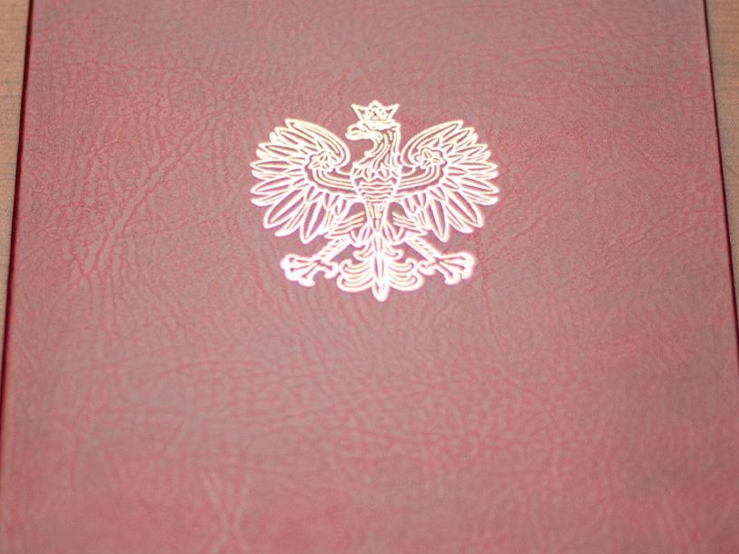 bordowa teczka ze złotym orłem, z prawj strony leży czarne pióro