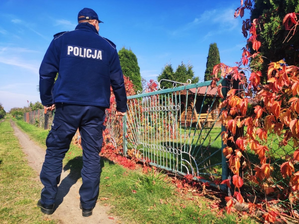 policjant stoi tyłem przy ogrodzeniu działkowym