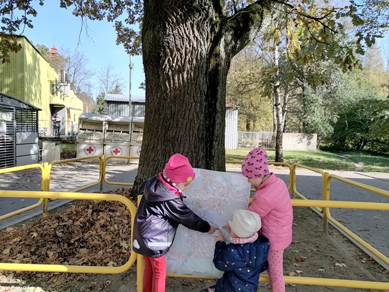  troje dzieci stoi przed dębem i trzyma mapę