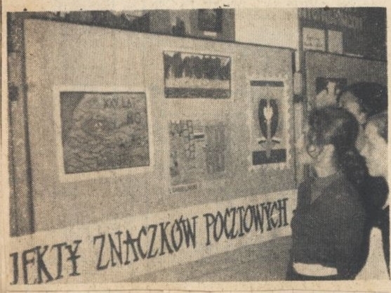 skan czarno-białego zdjęcia prasowego, na którym widoczny jest fragment wystawy projektów znaczków pocztowych oraz trzy osoby po prawej stronie kadru, które oglądają prace