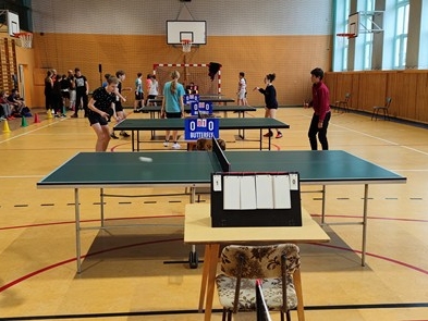 Młodzież gra w tenisa stołowego na sali gimnastycznej