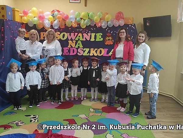 Pamiątkowe zdjęcie grupowe. Dzieci i nauczycielki oraz pani dyrektor stoją przed dekoracją okazjonalną.