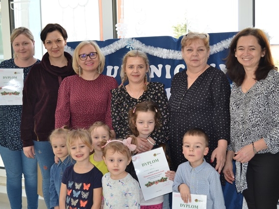 Zdjęcie przedstawia grupowe ustawienie uczestników Ekumenicznego Koncertu Kolęd: dzieci, pani dyrektor oraz panie nauczycielki.