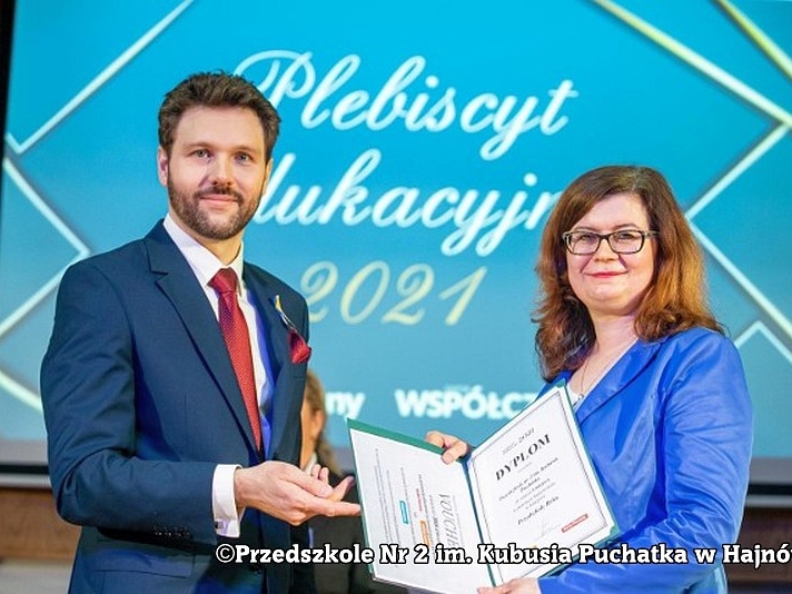 Na zdjęciu kobieta i mężczyzna na niebieskim tle kobieta trzyma teczkę z dokumentem.