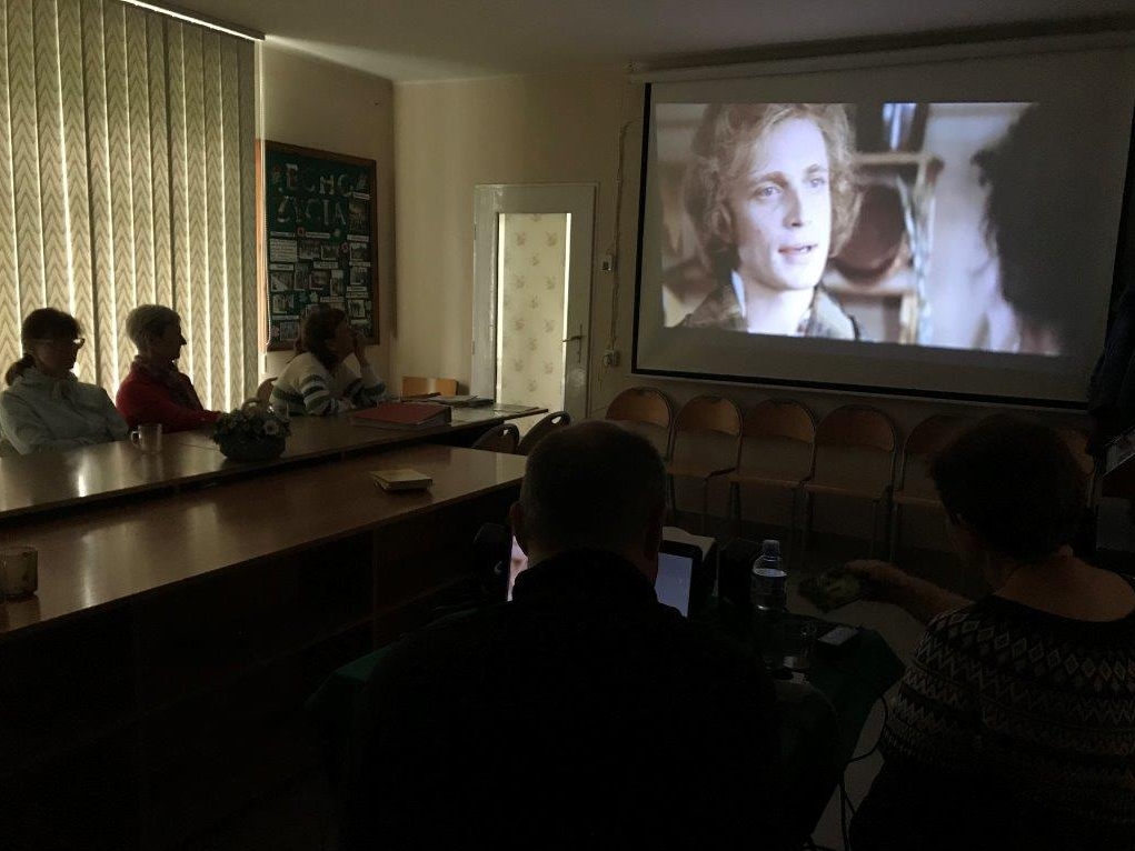 Kilka osób ogląda seans filmowy w przyciemnionej sali