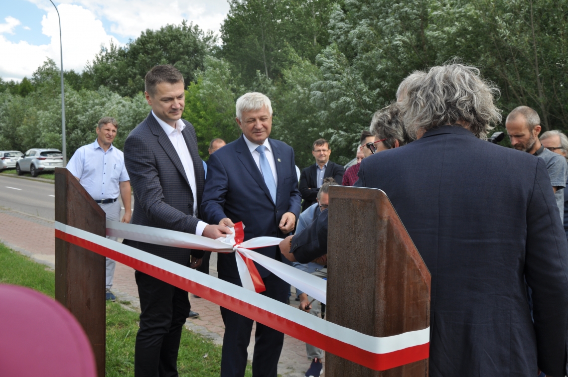 grupa ossób, uroczyście rozwiązuje wstęgę jako znak oficjalnego odsłonięcia rzeźby