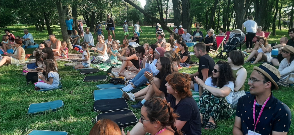 Publiczność siedzi na trawie.