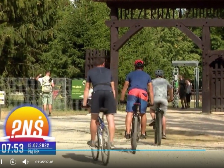 rowerzyście jadą w stronę  dużej drewnianej bramy "Rezerwatu żubrów"