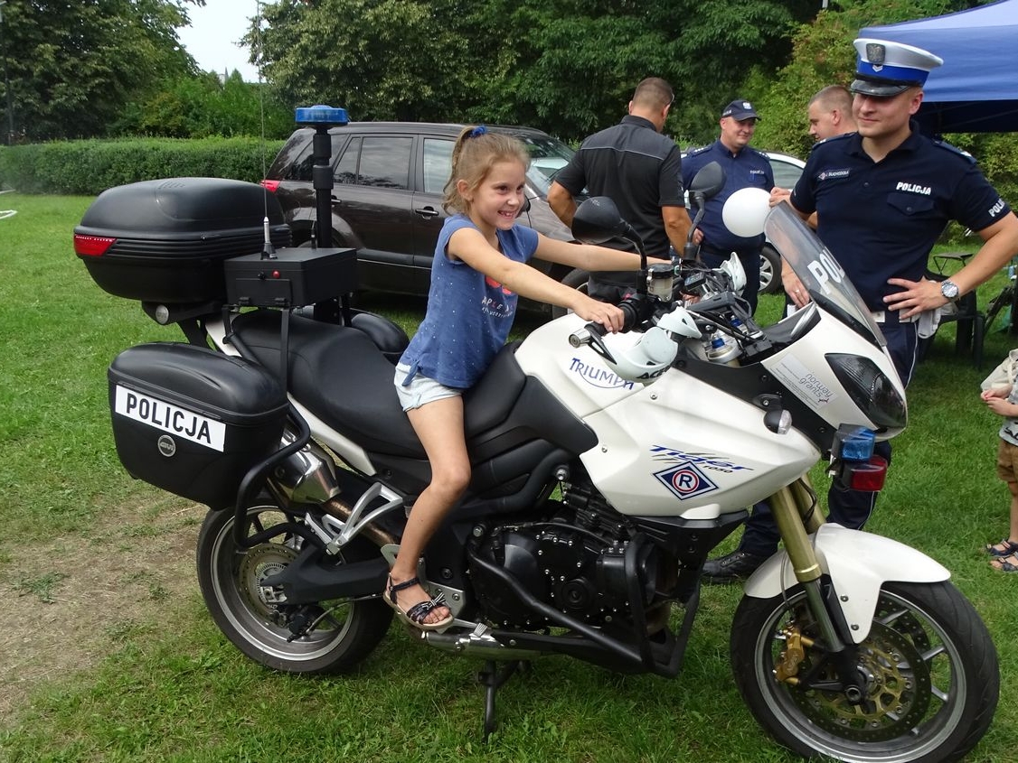 Dziewczynka siedzi na motocyklu policyjnym, obok stoi umundurowany policjant.