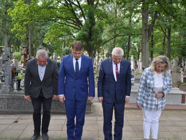 Sekretarz gminy, zastępca burmistrza, burmistrz i wicestarosta hajnowski oddają pokłon przed pomnikami poległych, w tle nagrobki cmentarza.