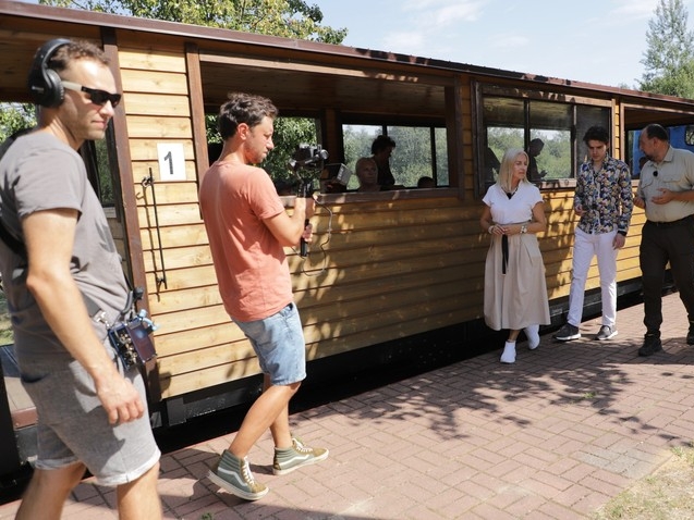 z lewej strony widać operatorów kameery, w prawej trzy osoby podczas nagrania. W tle widać kolejkę wąskotorową i Puszczę Białowieską