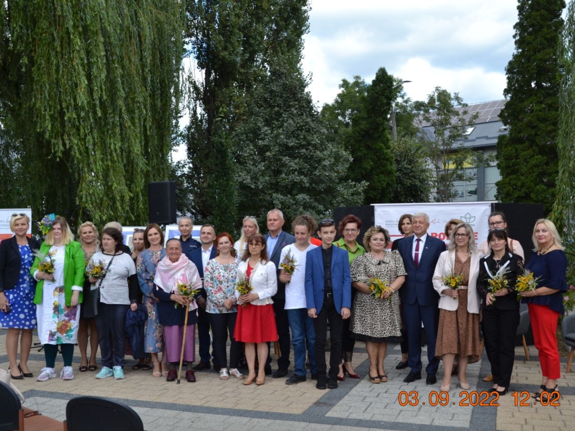 Grupa osób pozuje do zdjecia. W tle widać duże drzewa.