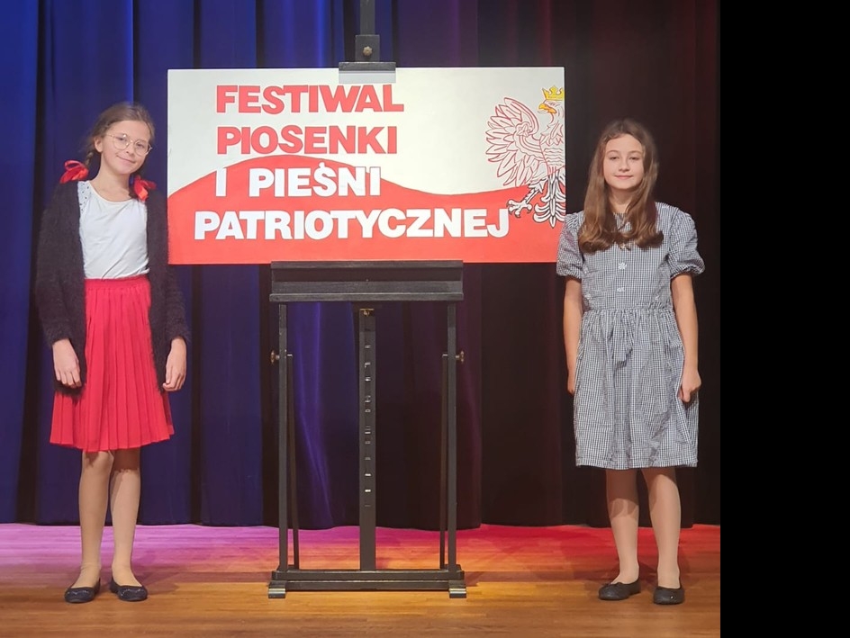 dwie dziewczynki stoją przy planszy z tytułem festiwalu