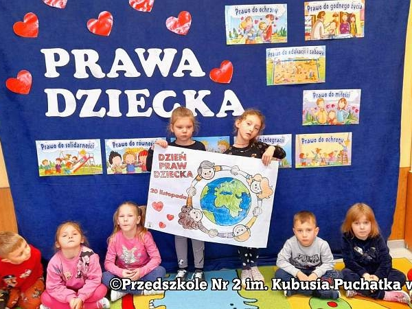 Dzieci siedzą na podłodze, za nimi granatowe tło z napisem: Prawa dziecka