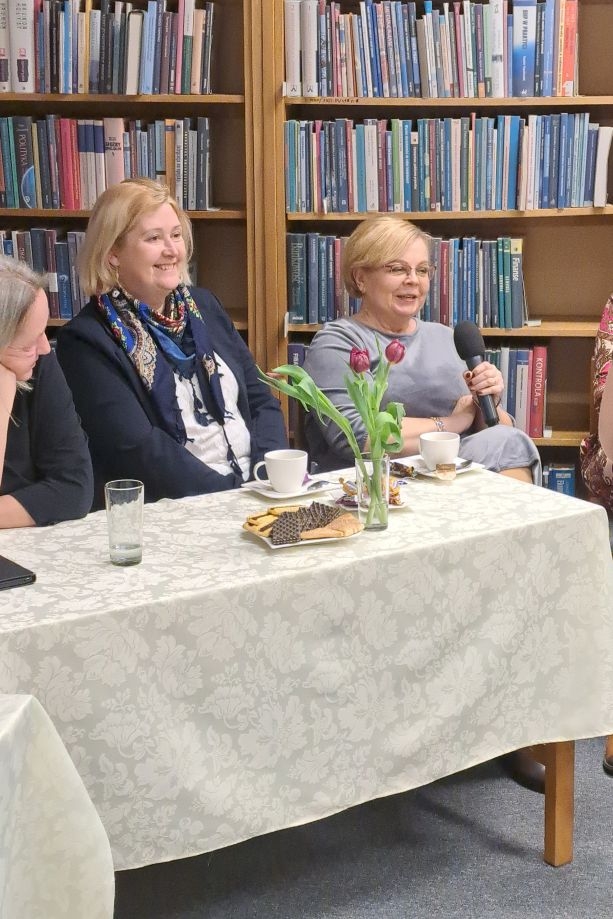 Kobiety siedzą za stołami nakrytymi białymi obrusami.