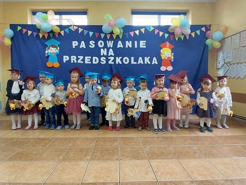grupa dzieci siedzi przez napisem Pasowanie na przedszkolaka