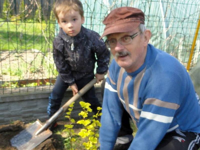 Mały chłopiec trzym łopatę, starszy meżczyzna zakopuje roślinkę. Obaj patrzą w stronę obiektywu