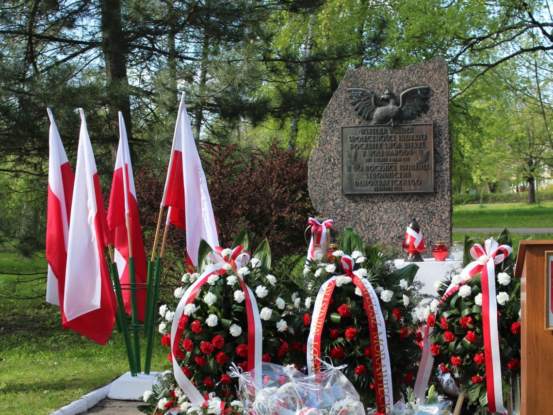 obelisk 3 Maja ze złożonymi kwiatami i stojącymi przy nim flagami Polski