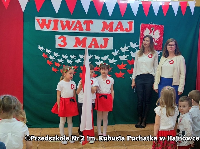 dwie dziewczynki trzymaja flage narodową. Obok stoi nauczycielka i pani dyrektor