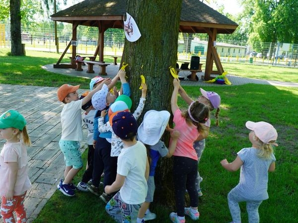 Dzieci zrywają banany zawieszone na drzewie.