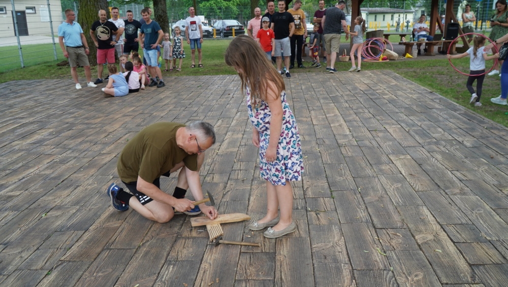 Mężczyzna trzyma młotek i drewno, obok stoi dziewczynka.