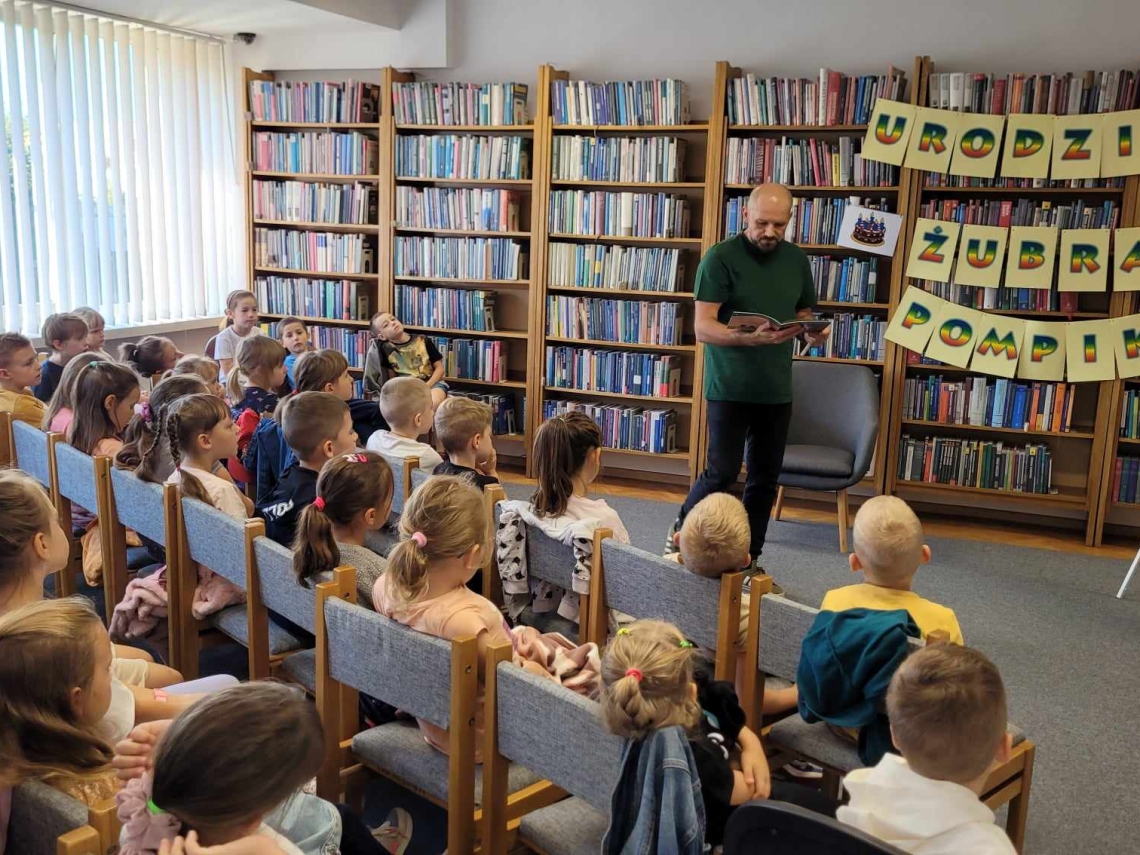 dzieci przybyłe do biblioteki na urodziny, przed nimi stoi autor przygód o żubrze Pompiku Tomasz Samojlik