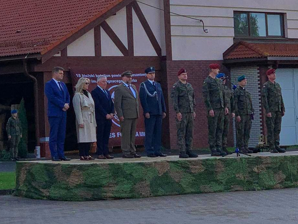 dziesięć osób stoi na podwyższeniu. Siedem z nich jest w mundurach.