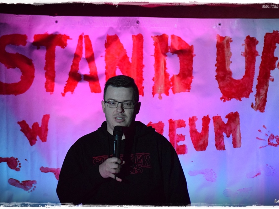 mężczyzna z mikrofonem. W tle widać podświetlony napis STAND UP 