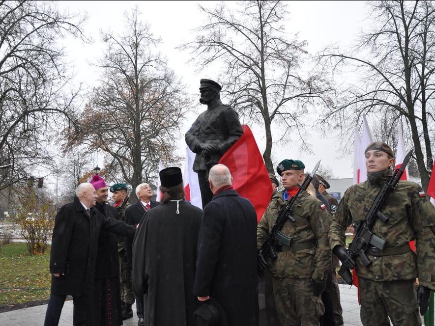 zaproszone osobistości osłaniaja pomnik. Obok żołnierze pełnią wartę. 