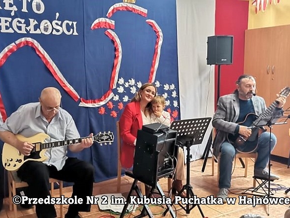 dwaj panowie grają na gitarach, kobieta trzyma na kolanach dziecko