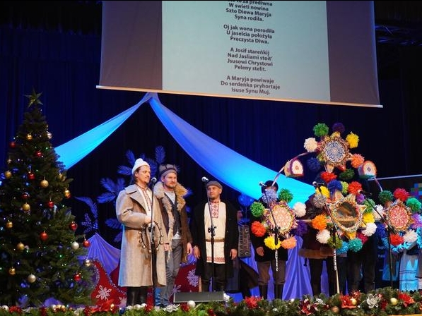 grupa kolędników z gwiazdę stoi na scenie przy choince.