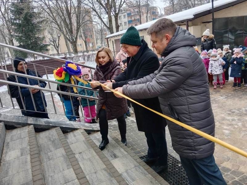  przedstawia pana Burmistrza Miasta Hajnówka, zastępcę Burmistrza Miasta Hajnówka i panią Dyrektor Przedszkola nr 5 w Hajnówce przecinających wstęgę zawieszoną na schodach prowadzących do przedszkola.