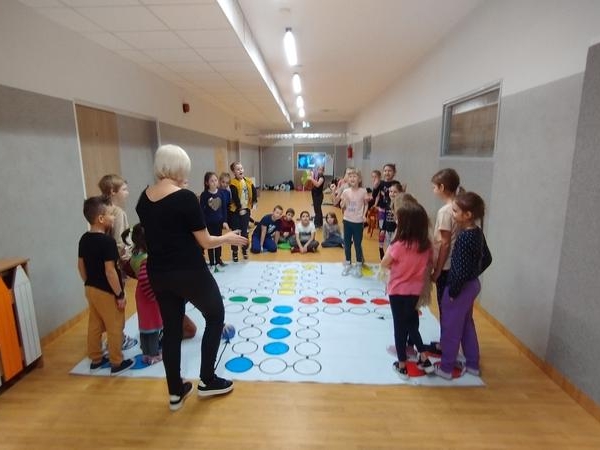 dzieci stoją przy wielkiej planszy do gry chińczyk