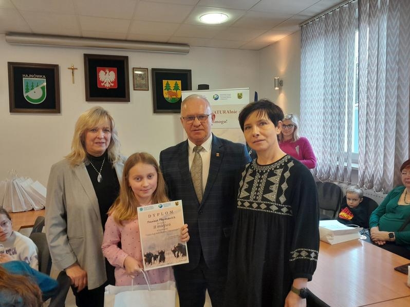 laureatka konkursu trzyma duplom i torbę z nagrodami. Za nią stoją organizatorzy konkursu i władze powiatu