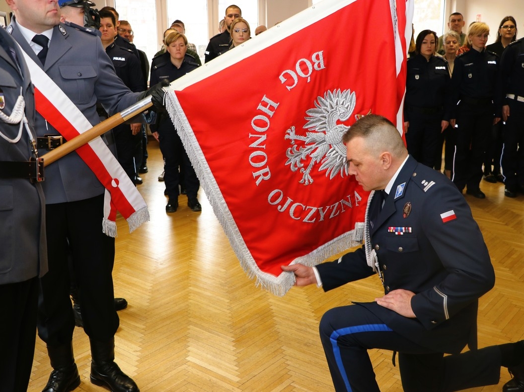 mężczyzna w mundurze klęka przy sztandarze z napisem: "Bóg Honor Ojczyzna"