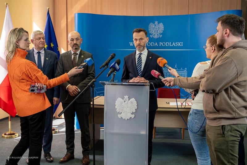 mężczyzn przemawia do mikrtofonów. Obok stoją burmistrzowie oraz prasa.