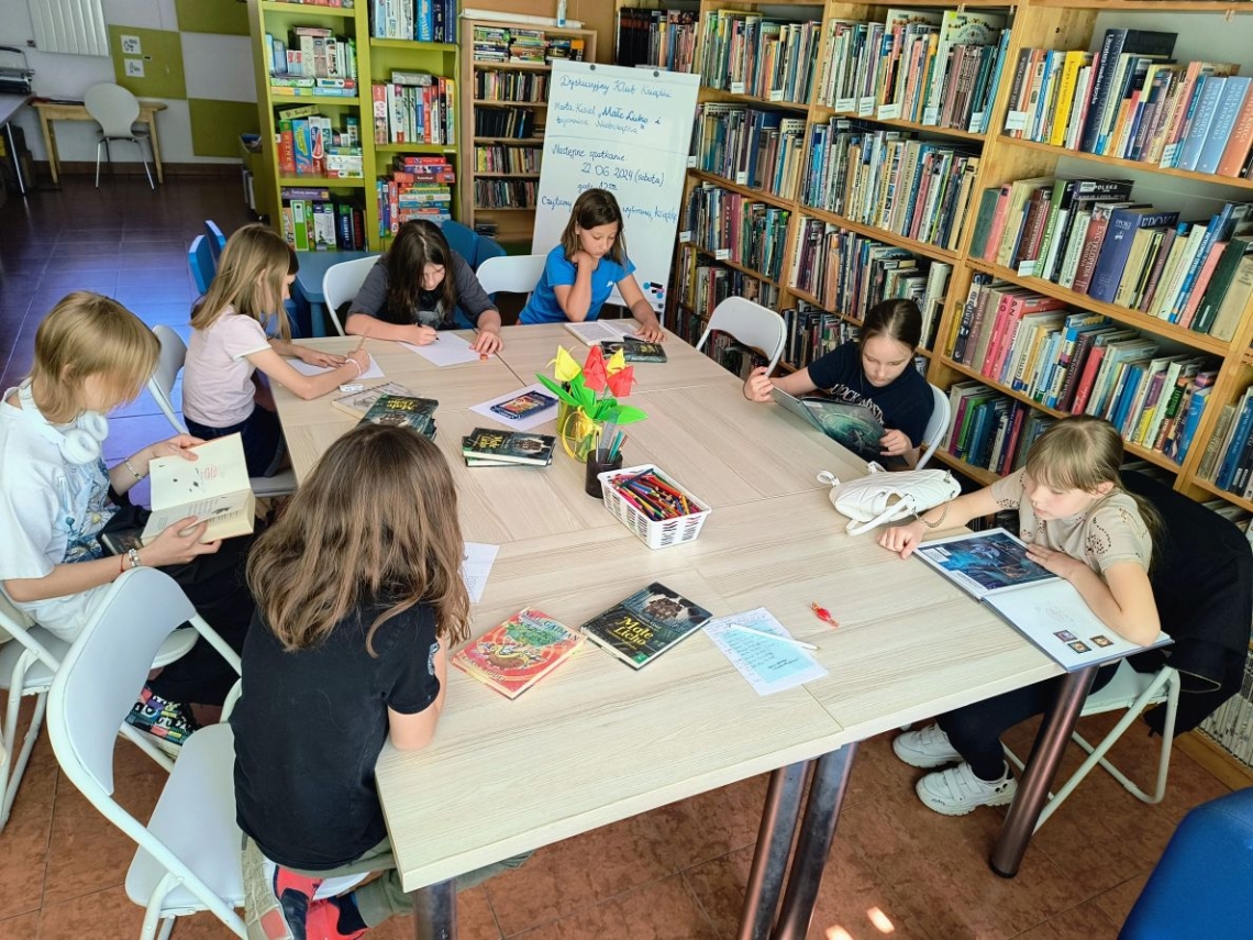 dzieci siedzące przy stole w bibliotece. Na stole leżą książki