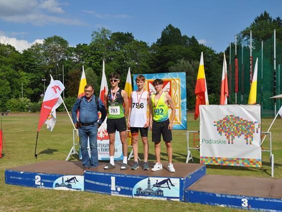 trzech zawodników stoi z trenerem na podium