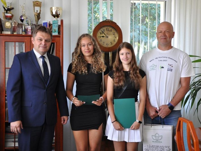 dziewczęta trzymają teczki z gratulacjami, obok stoi trener z torbą upominkową oraz burmistrz