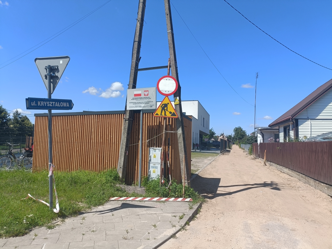 zdjęcie trwajacej inwestycji drogowej wraz z tablicą informacyjną o dofinansowaniu