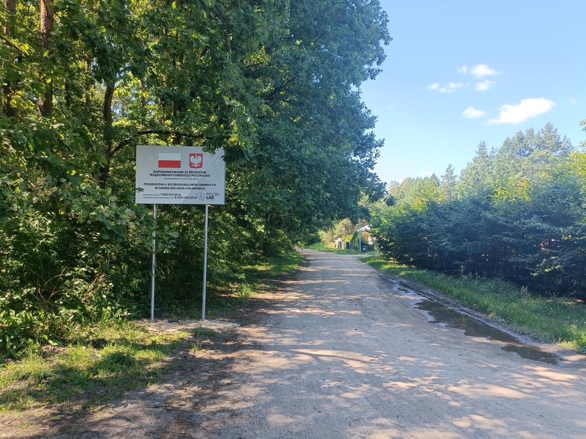zdjęcie trwajacej inwestycji drogowej wraz z tablicą informacyjną o dofinansowaniu