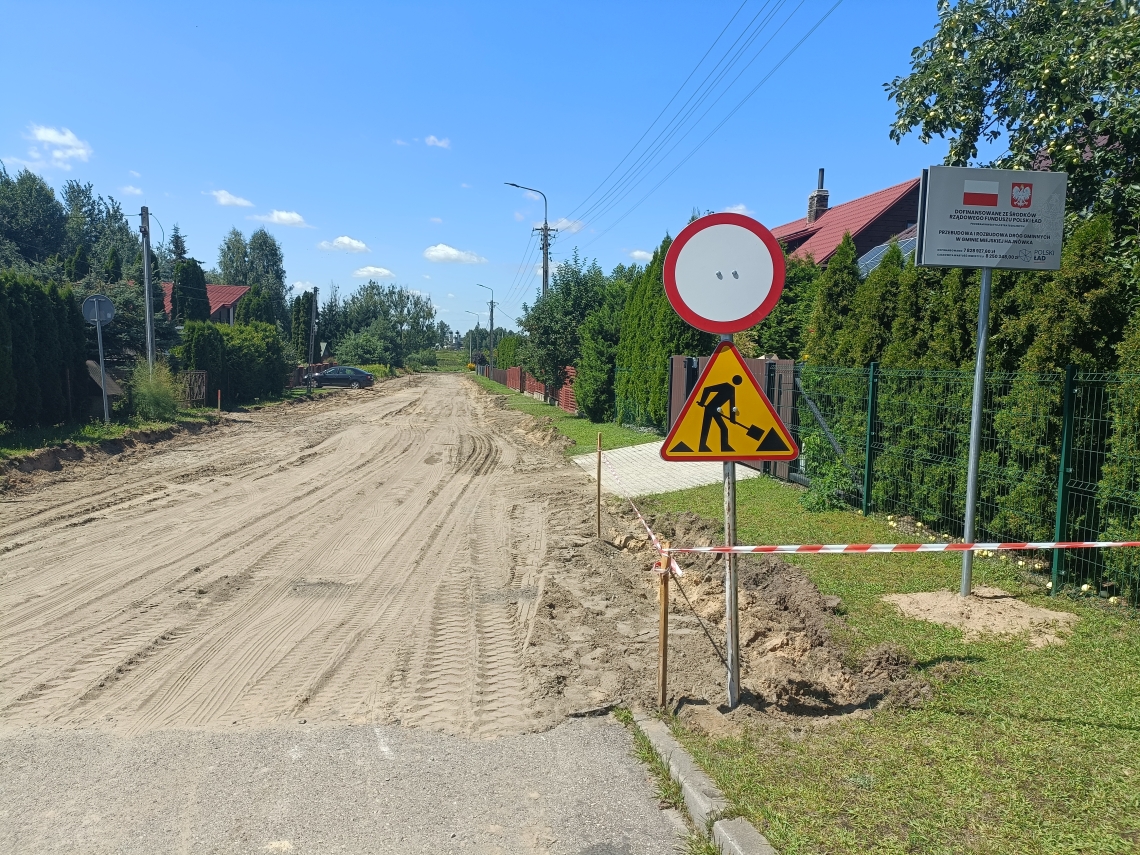 zdjęcie trwajacej inwestycji drogowej wraz z tablicą informacyjną o dofinansowaniu