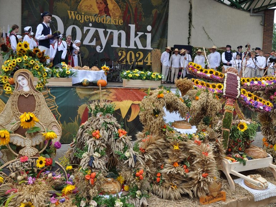 zespół występuje na scenie. Pod scena ustawione wieńce dożynkowe. 