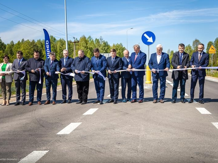 czternaście osób stoi na drodze i przecina wstęgię